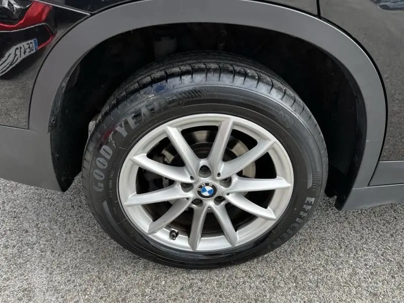 Gros plan sur la roue avant gauche d’un BMW X1 noir métal de 2017 avec jante alliage argent et pneu Goodyear.