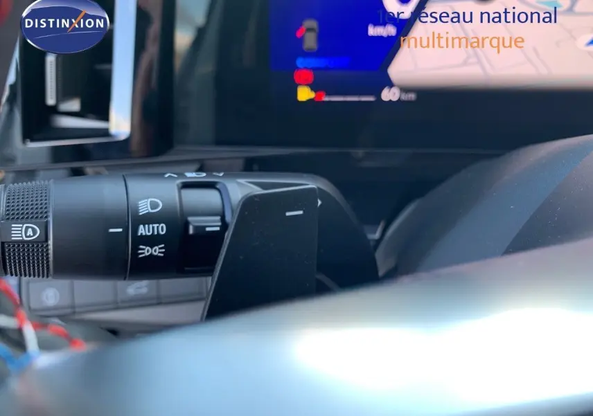 Gros plan sur la commande des phares et le volant d'un Renault Austral 2024 hybride avec tableau de bord numérique allumé.