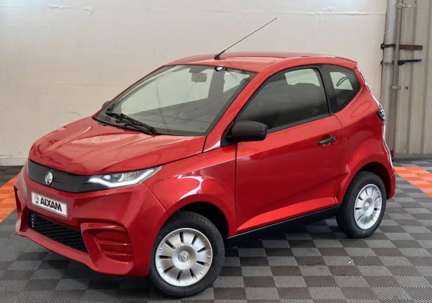 Vue 3/4 avant d'une Aixam Ambition E City Pack rouge électrique avec rétroviseur caméra côté gauche en intérieur showroom.