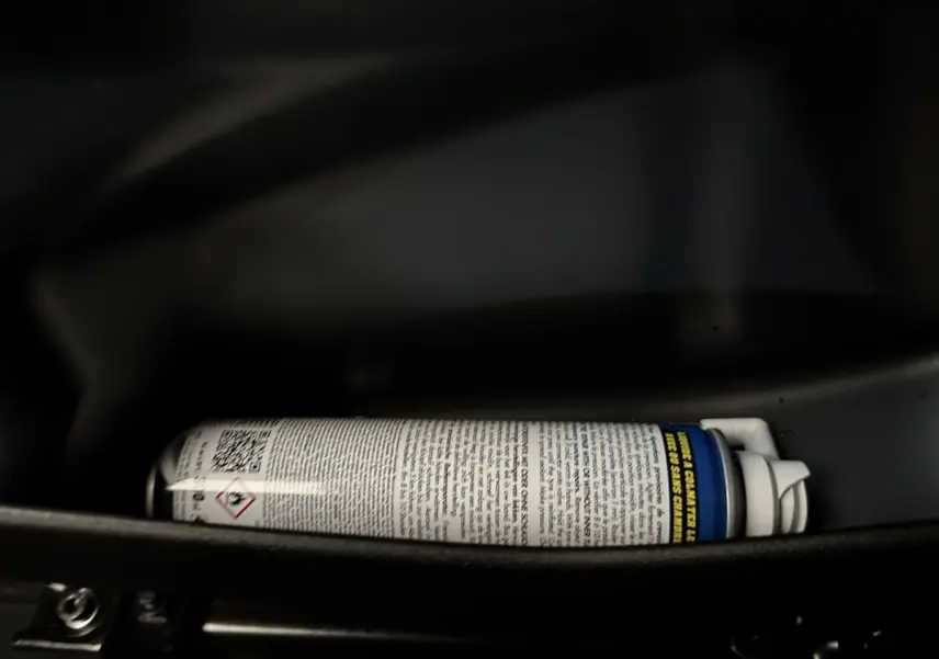 Gros plan sur une bombe aérosol dans le rangement intérieur d'une Aixam Ambition E City Pack rouge 2025 électrique.