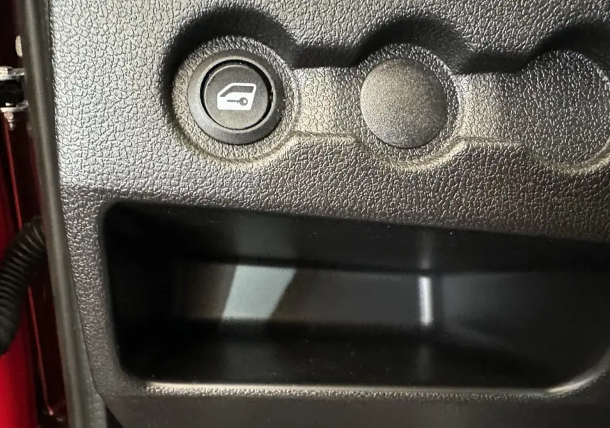 Bouton d'ouverture du coffre sur la console intérieure noire d'une Aixam Ambition E City Pack rouge, côté conducteur.