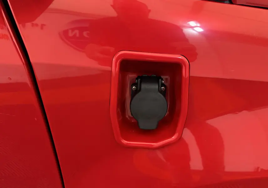 Prise de recharge électrique en gros plan sur la portière rouge côté conducteur de l'Aixam Ambition E City Pack 2025.