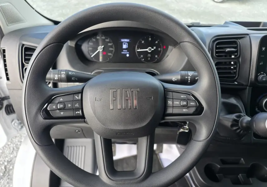 Vue intérieure du poste de conduite du Fiat Ducato Fourgon blanc, avec volant et commandes au tableau de bord visibles.