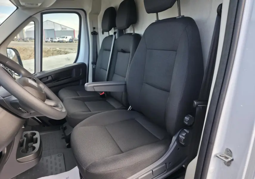 Vue intérieure côté conducteur du Fiat Ducato Fourgon blanc 2025, montrant les sièges tissu noir et le volant.