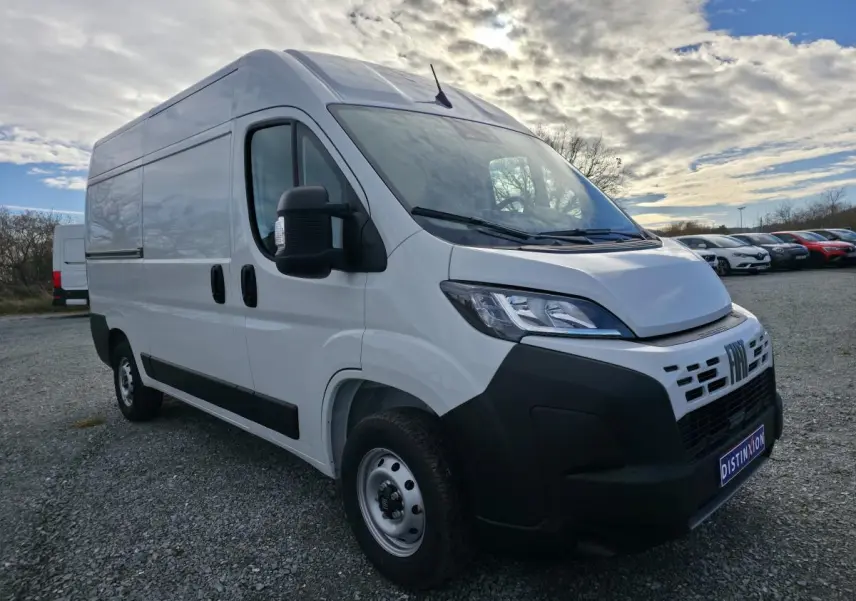 Vue 3/4 avant d'un FIAT Ducato Fourgon blanc avec pare-chocs noirs et roues acier sur parking extérieur.
