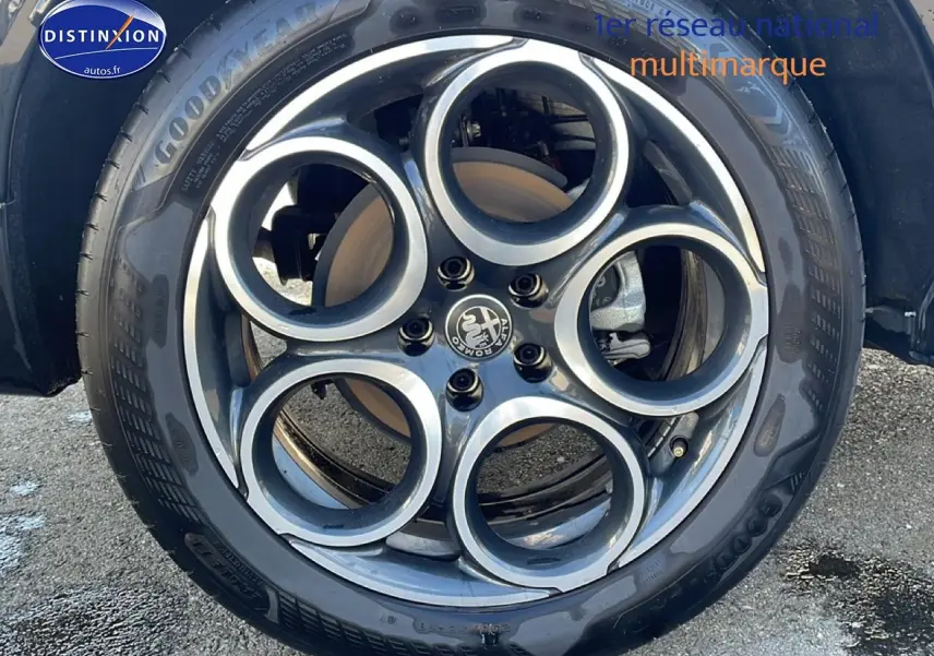 Gros plan sur la jante alu noire et argentée à cinq cercles de l'Alfa Romeo Tonale blanc, roue avant droite visible.