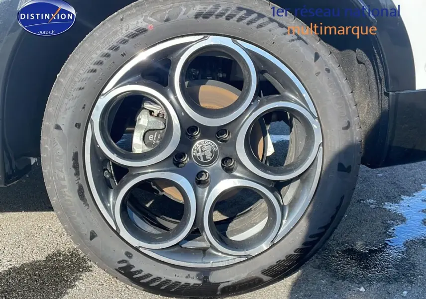 Gros plan sur la jante alu noire et argentée de l'Alfa Romeo Tonale blanche, roue avant droite visible.