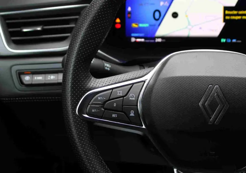 Gros plan sur le volant perforé noir du Renault Symbioz 2025 avec commandes intégrées et écran numérique en arrière-plan.