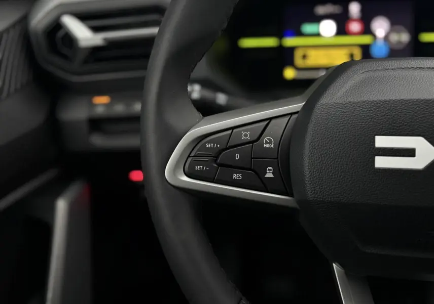 Gros plan sur le volant noir du Dacia Duster 2026 avec commandes intégrées et tableau de bord digital flou en arrière-plan.