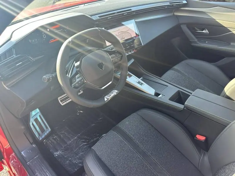 Vue intérieure côté conducteur de la Peugeot 308 rouge Elixir, avec volant multifonction et écran tactile central.