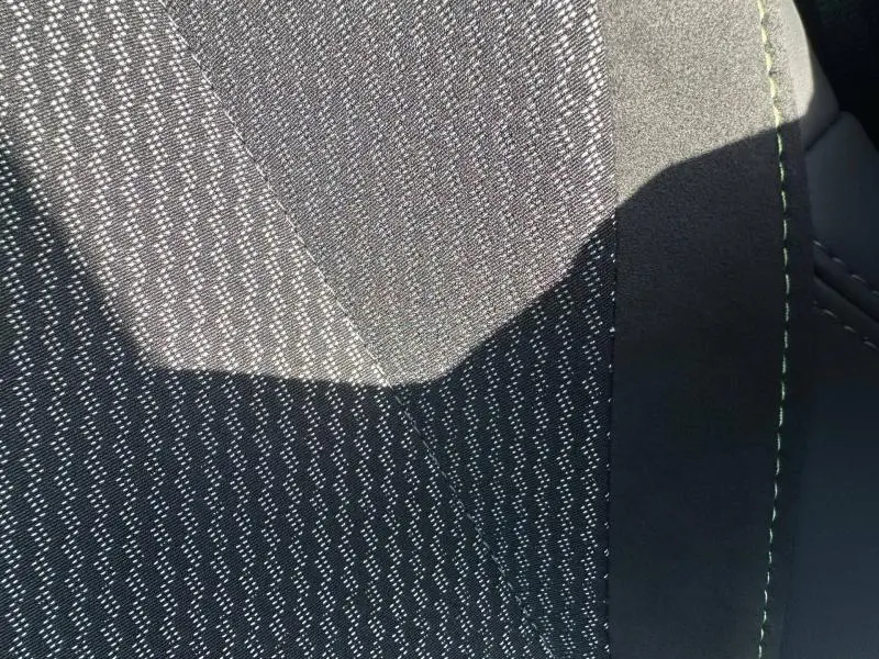 Gros plan sur le tissu noir à motifs blancs et surpiqûres vertes du siège avant du Peugeot 308 Rouge Elixir.