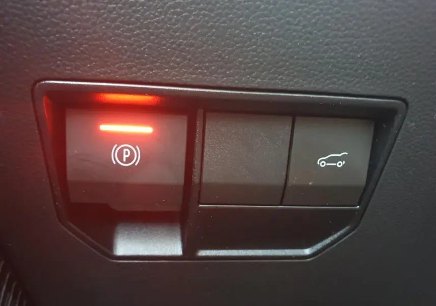Gros plan sur les boutons de commande du frein de parking et ouverture du coffre dans l’habitacle du Dacia Bigster gris schiste.