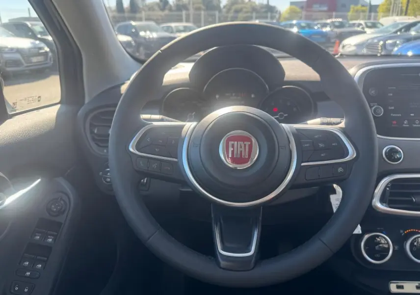 Vue intérieure centrée sur le volant du Fiat 500X MY23 avec tableau de bord et commandes visibles.