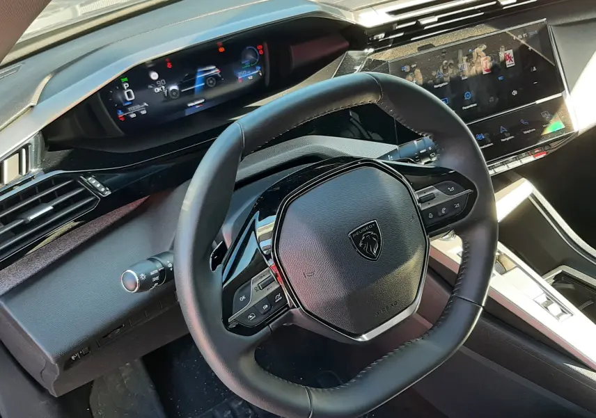 Vue intérieure du volant et tableau de bord numérique de la Peugeot 308 SW Hybrid 2025, ambiance moderne et finition noire.