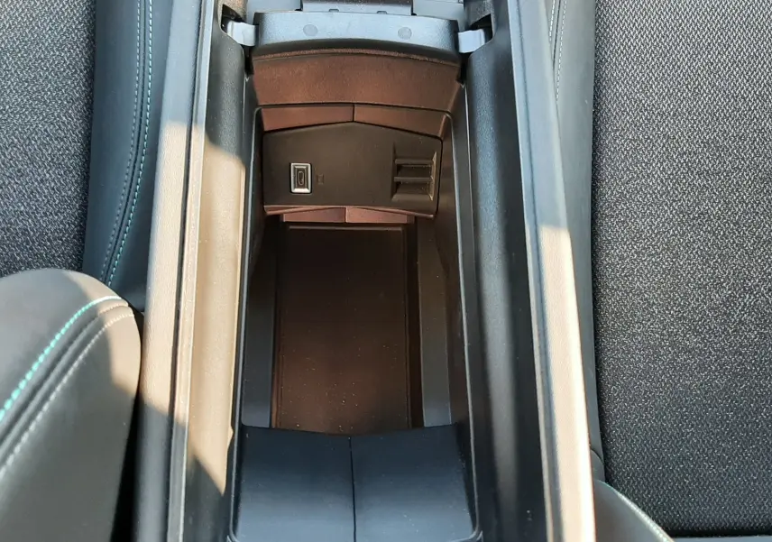 Vue plongeante sur le rangement central ouvert de la Peugeot 308 SW Hybrid 2025, avec prise USB visible et sellerie noire.