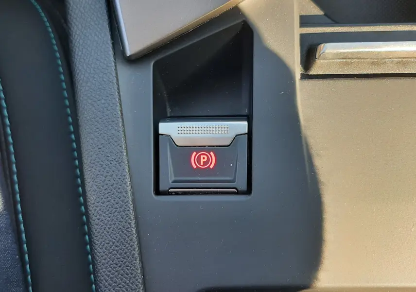 Gros plan sur le bouton de frein à main électronique rouge dans la console centrale d'une Peugeot 308 SW gris selenium.