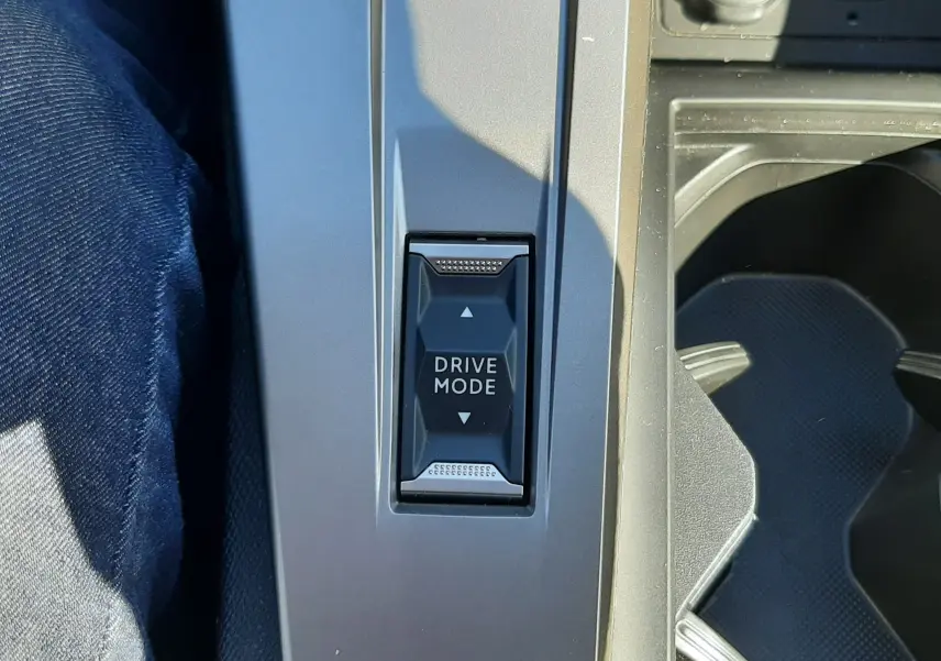 Vue rapprochée du bouton Drive Mode sur la console centrale grise du Peugeot 308 SW Hybrid 2025, avec prise 12V et port USB visibles.