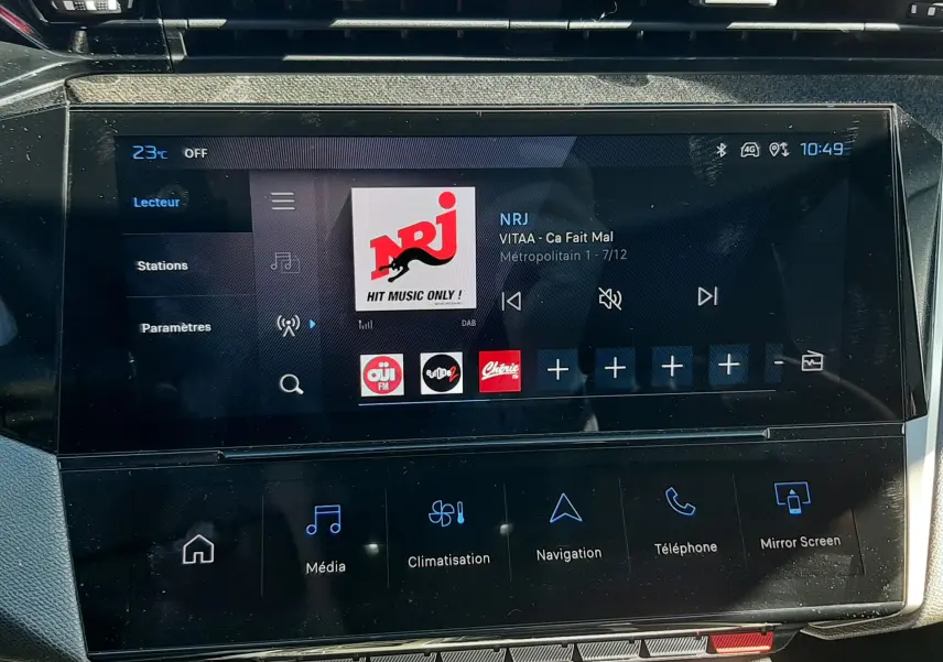 Écran tactile central de la Peugeot 308 SW Hybrid 2025 affichant la radio NRJ, avec commandes multimédia et climatisation.