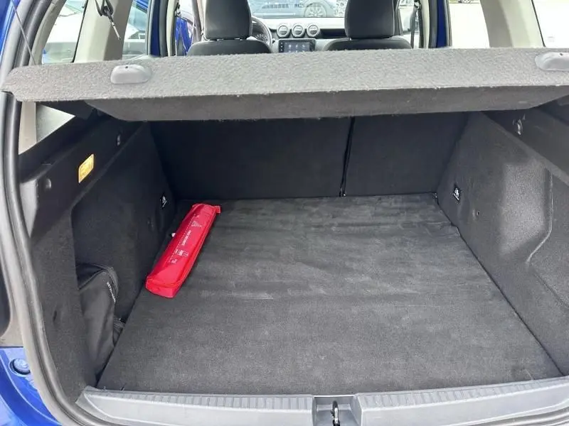 Vue intérieure du coffre ouvert d'un Dacia Duster bleu métal 2022, avec tapis noir et trousse de secours rouge visible.