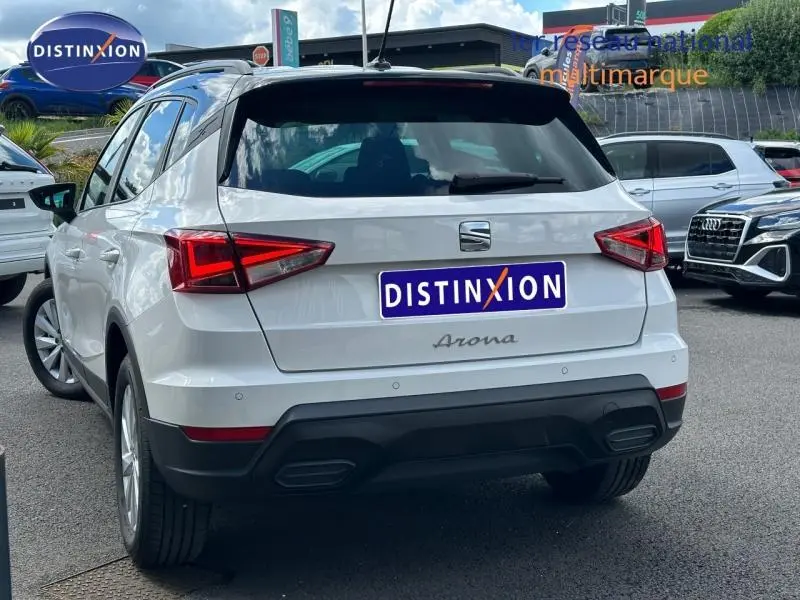 Vue 3/4 arrière d'un SEAT Arona blanc Candy avec toit noir Minuit, feux arrière LED et double sortie d'échappement intégrée.