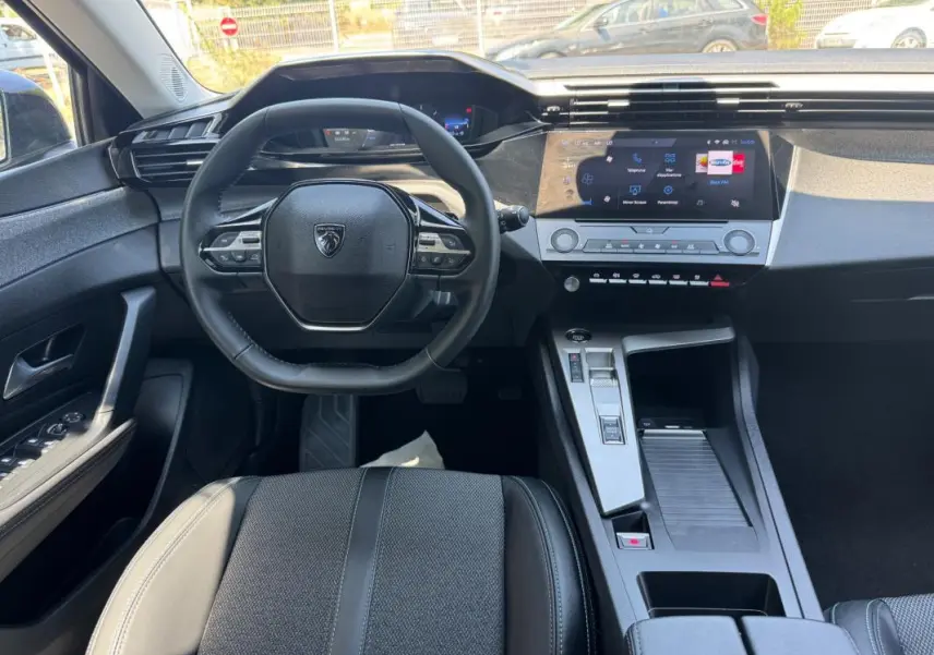 Vue intérieure avant de la Peugeot 308 gris, montrant le volant multifonction, l’écran tactile central et la console moderne.