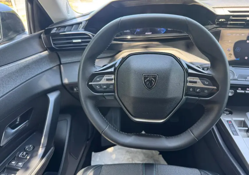 Vue intérieure centrée sur le volant noir de la Peugeot 308 gris avec commandes intégrées et tableau de bord numérique.