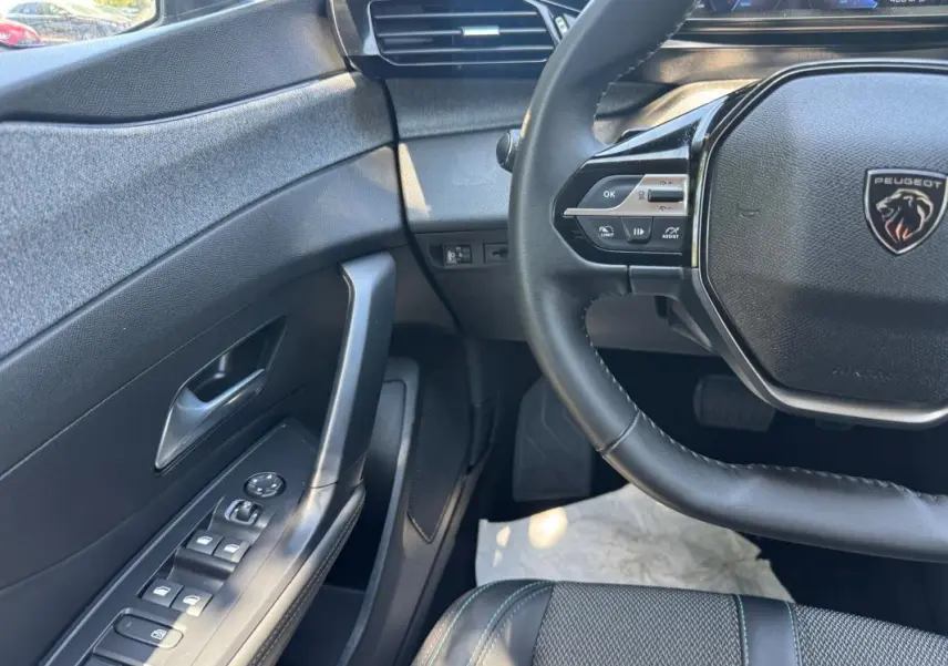 Vue intérieure côté conducteur de la Peugeot 308 gris, avec volant multifonction et commandes des vitres électriques.