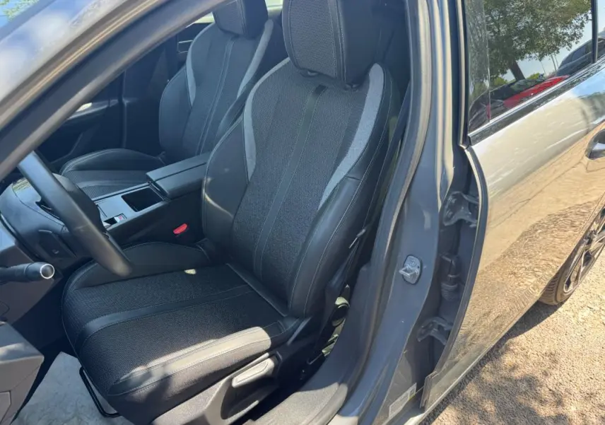 Vue intérieure côté conducteur de la Peugeot 308 gris 2025, mettant en valeur les sièges en tissu et cuir avec accoudoir central.