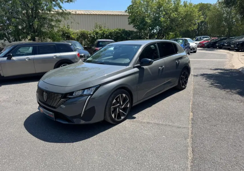 PEUGEOT 308 gris en 3/4 avant droit, avec jantes alliage noires et calandre distinctive moderne.