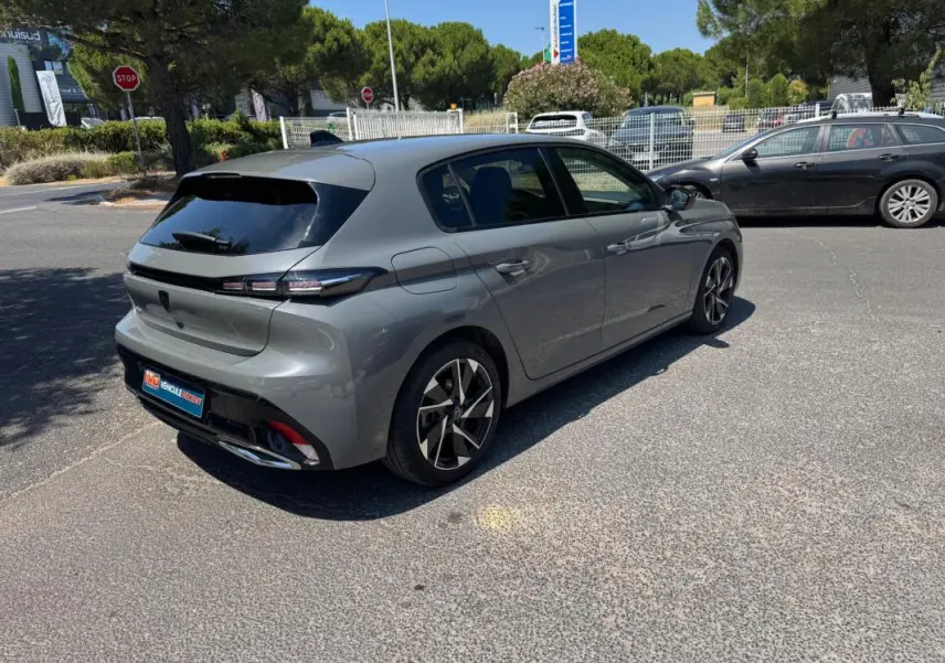 Peugeot 308 gris vue 3/4 arrière droit, jantes alliage 17 pouces et vitres arrière teintées.
