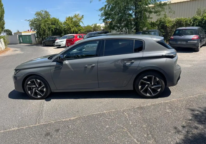 Vue de profil côté gauche d'une Peugeot 308 gris métallisé 2025 avec jantes alliage 17 pouces sur parking extérieur.