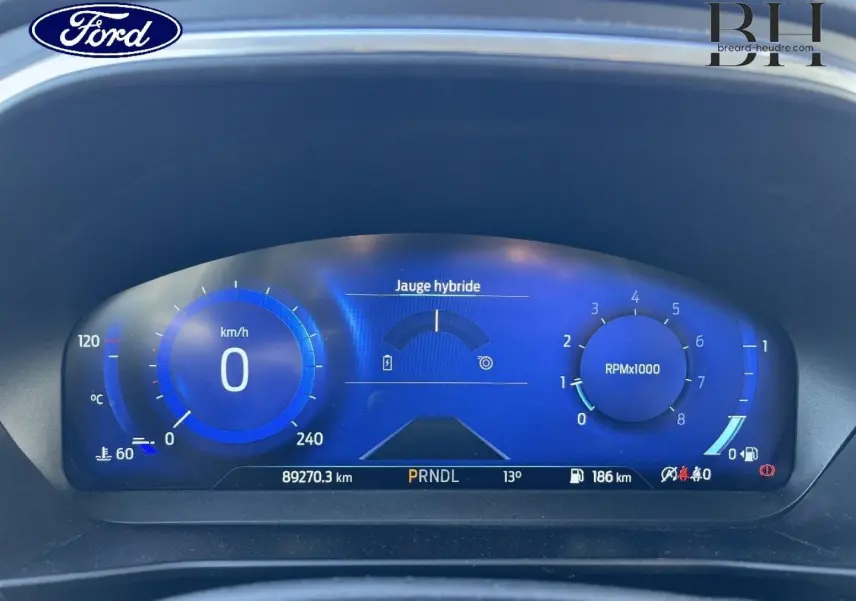 Vue rapprochée du tableau de bord numérique bleu de la Ford Focus Titanium X 2022, affichant jauge hybride et compte-tours.