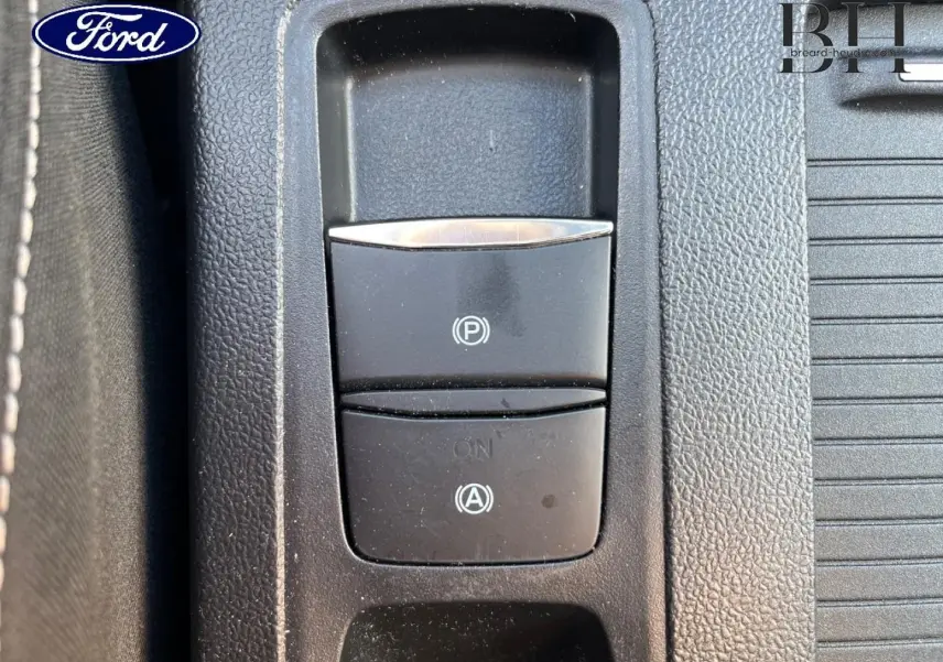 Gros plan sur les commandes de frein à main électronique et d'aide au démarrage en côte dans la console centrale noire d'une Ford Focus.