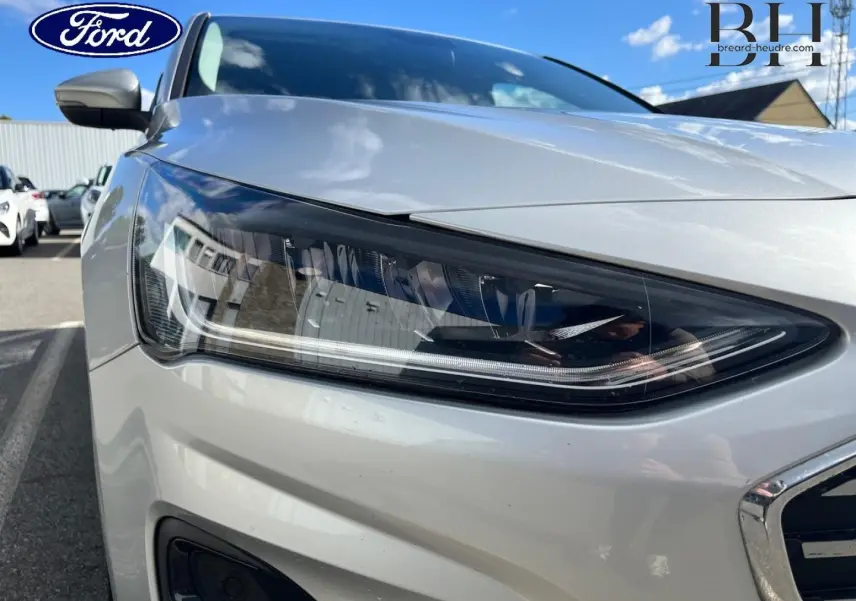 Gros plan sur le phare avant droit d'une Ford Focus gris lunaire métallisé, soulignant les détails modernes du bloc optique.