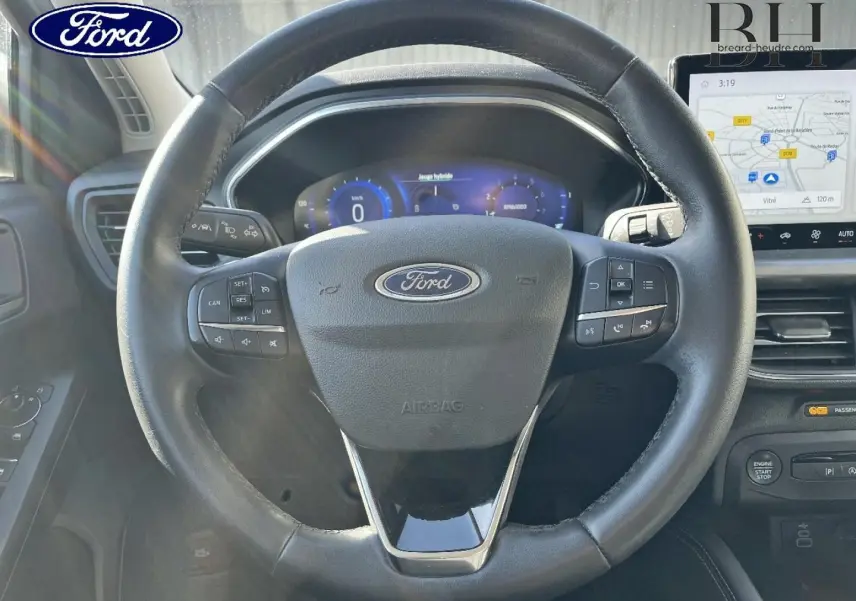 Vue rapprochée du volant en cuir noir de la Ford Focus 2022 avec commandes intégrées et écran tactile GPS visible.