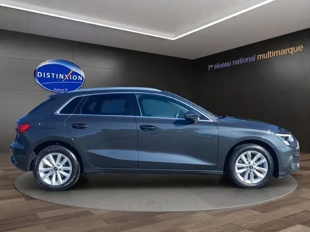 Profil côté droit de l'Audi A3 Sportback gris Manhattan avec vitres arrière surteintées dans un showroom moderne.