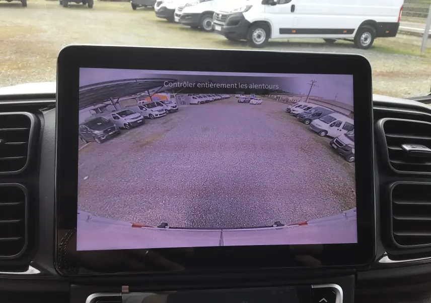 Vue depuis l'écran de recul du Peugeot Boxer Fourgon blanc, montrant un parking avec plusieurs véhicules utilitaires.