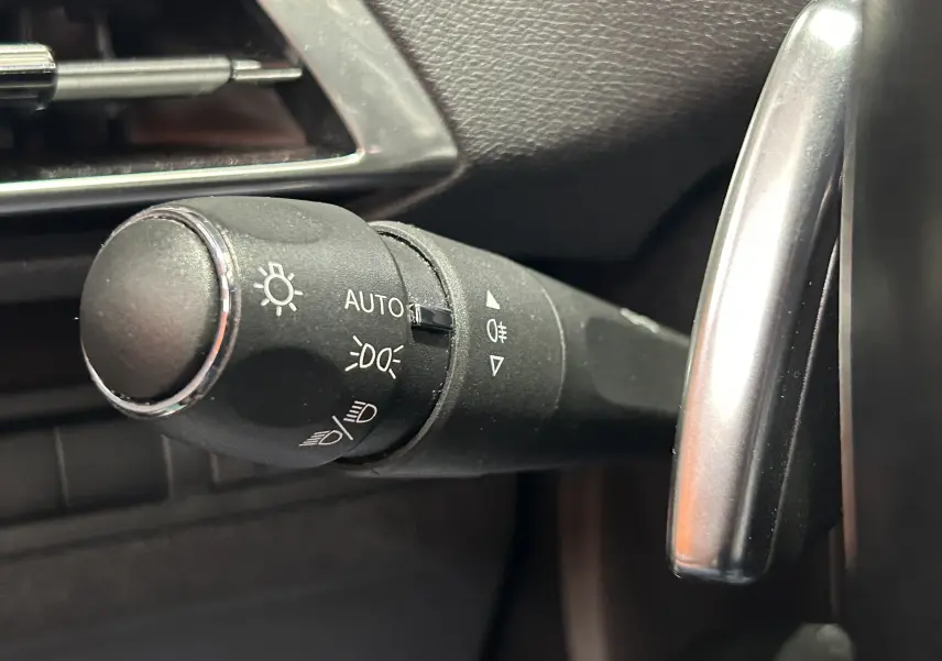 Gros plan sur la commande des phares à gauche du volant dans l’habitacle noir du Peugeot 3008 gris 2022.