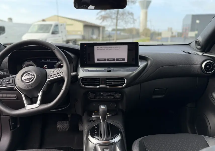 Vue intérieure avant du Nissan Juke 2025, tableau de bord noir avec écran tactile central et volant multifonctions.