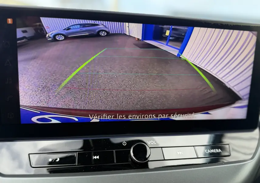 Vue caméra de recul montrant un parking avec un véhicule gris garé à gauche, affichage sur écran intérieur.