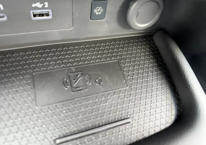 Gros plan sur la console centrale noire du Nissan Juke 1.6 Hybrid 2025, montrant la zone de recharge sans fil et ports USB.