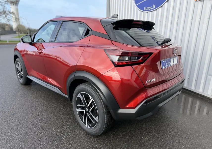 Vue 3/4 arrière droite du Nissan Juke rouge Fuji 2025 avec jantes alliage noires et toit noir contrasté.
