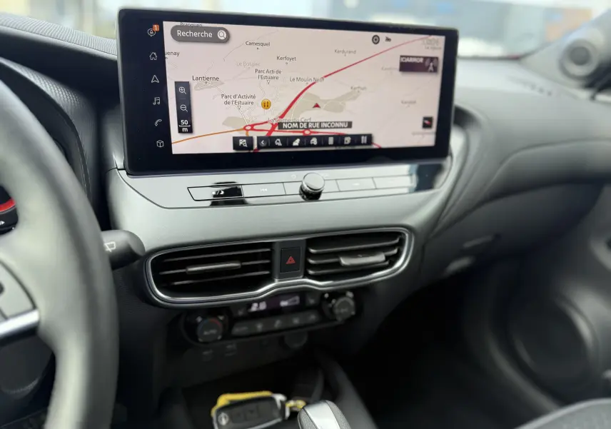 Vue intérieure du tableau de bord du Nissan Juke 2025, avec écran tactile de navigation et commandes de climatisation visibles.