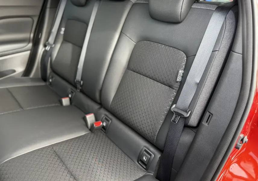 Vue rapprochée des sièges arrière noirs avec ceinture grise du Nissan Juke rouge Fuji, version hybride 2025.