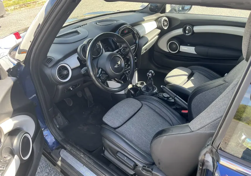 Intérieur côté conducteur d’une MINI Cabriolet bleu 2017, sellerie tissu/cuir gris noir avec tableau de bord moderne.