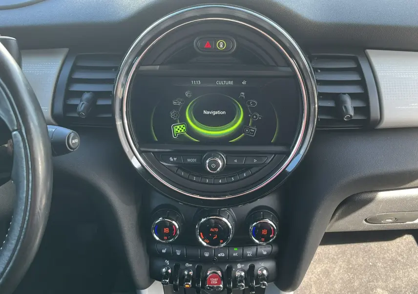 Vue rapprochée du tableau de bord central de la MINI Cabriolet bleu, avec écran de navigation circulaire et commandes climatisation.