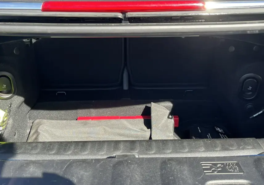 Coffre ouvert d’une MINI Cabriolet F57 Cooper S bleu, vue plongeante sur l’espace de rangement avec accessoires visibles.