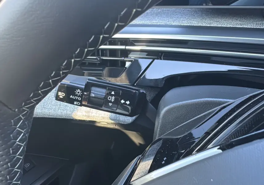 Gros plan sur la commande des feux et clignotants à gauche du volant cuir du Peugeot 3008 New Hybrid 2025.