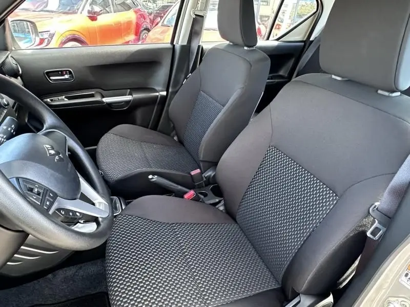 Vue intérieure côté conducteur de la Suzuki Ignis beige 2023, montrant les sièges avant en tissu noir à motifs.