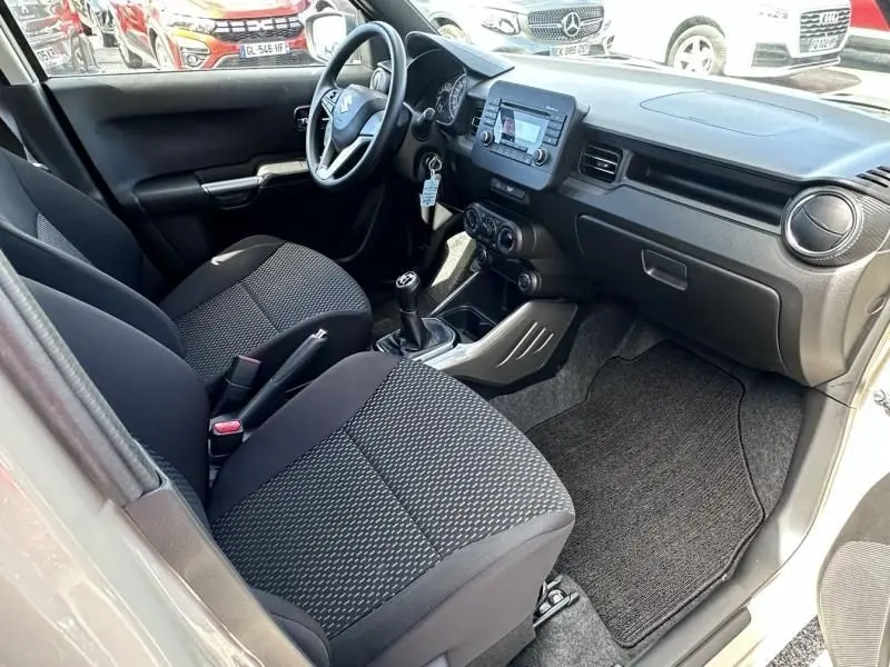 Vue intérieure côté conducteur de la Suzuki Ignis beige 2023, montrant le tableau de bord et la boîte manuelle.